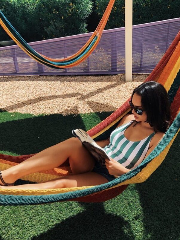 A brunette woman sits in a colorful hammock reading